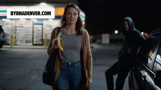Woman holding a banana walking by a man in a hood in the dark.