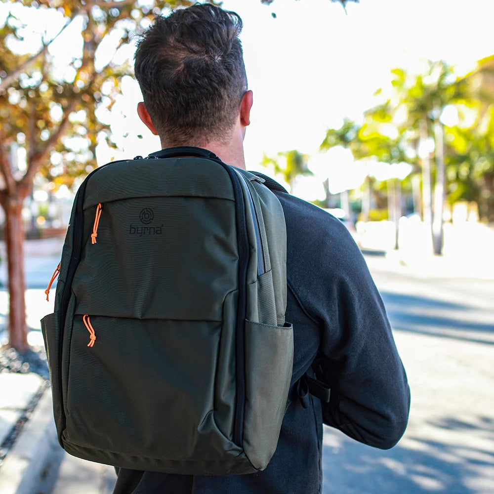 Person wearing a green backpack with Byrna branding outdoors.