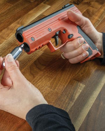 Person adding CO2 into a Byrna SD launcher over a wood table.