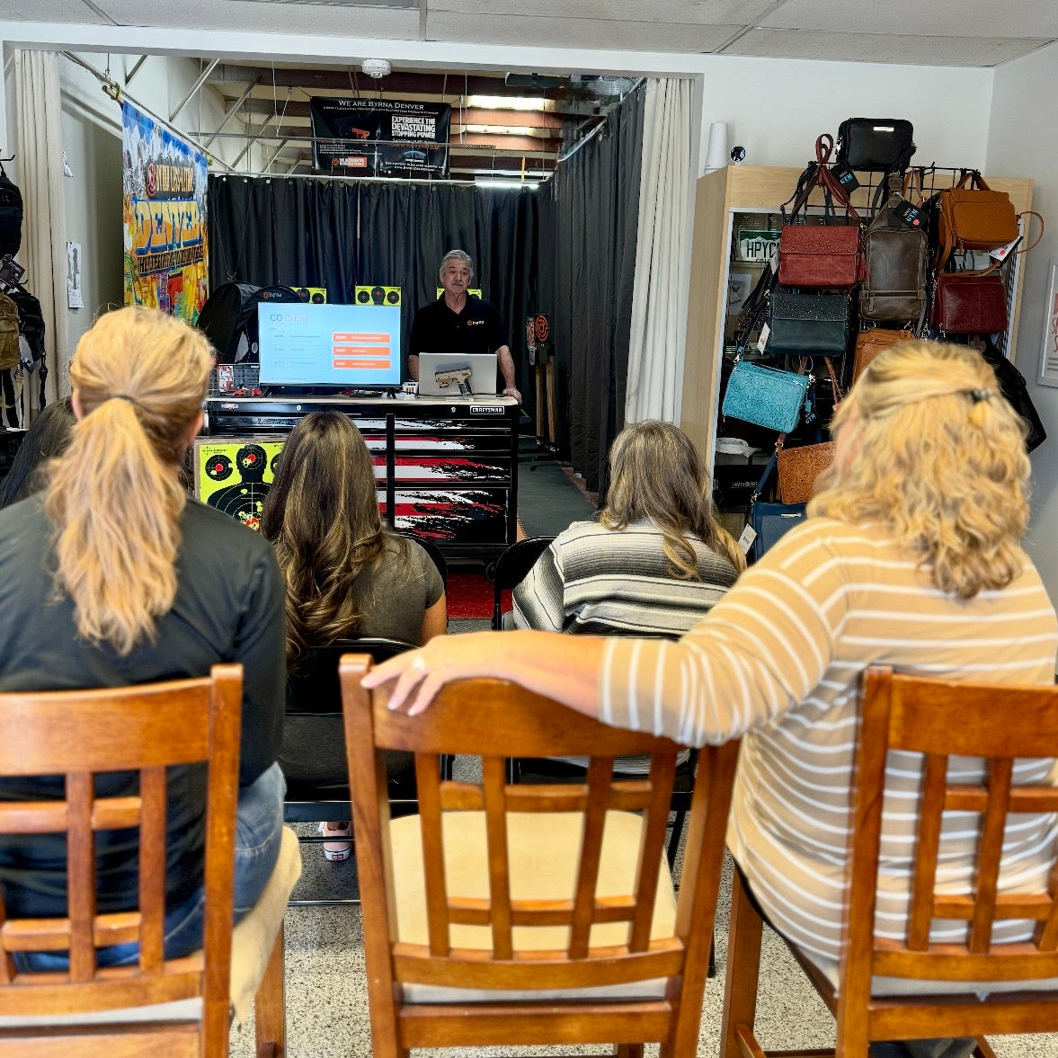 Byrna Denver owner, Bill, giving an educational presentation to an audience in the store with chairs and a screen.